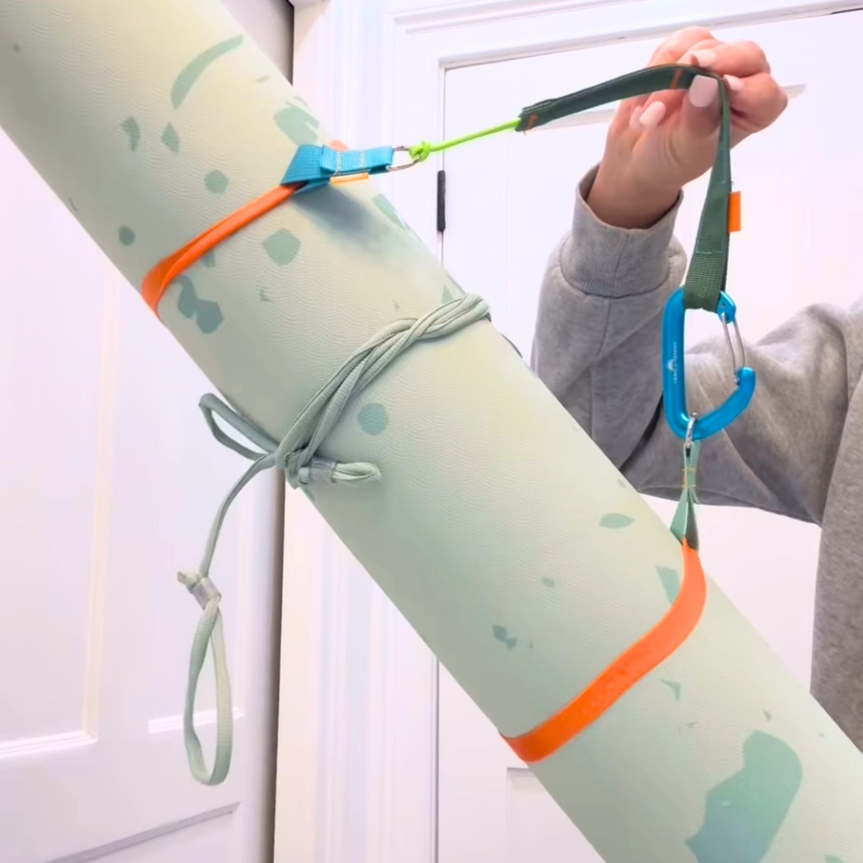 a young woman holds a yoga mat secured by two chameleon rings and one trail tether to form a carry strap